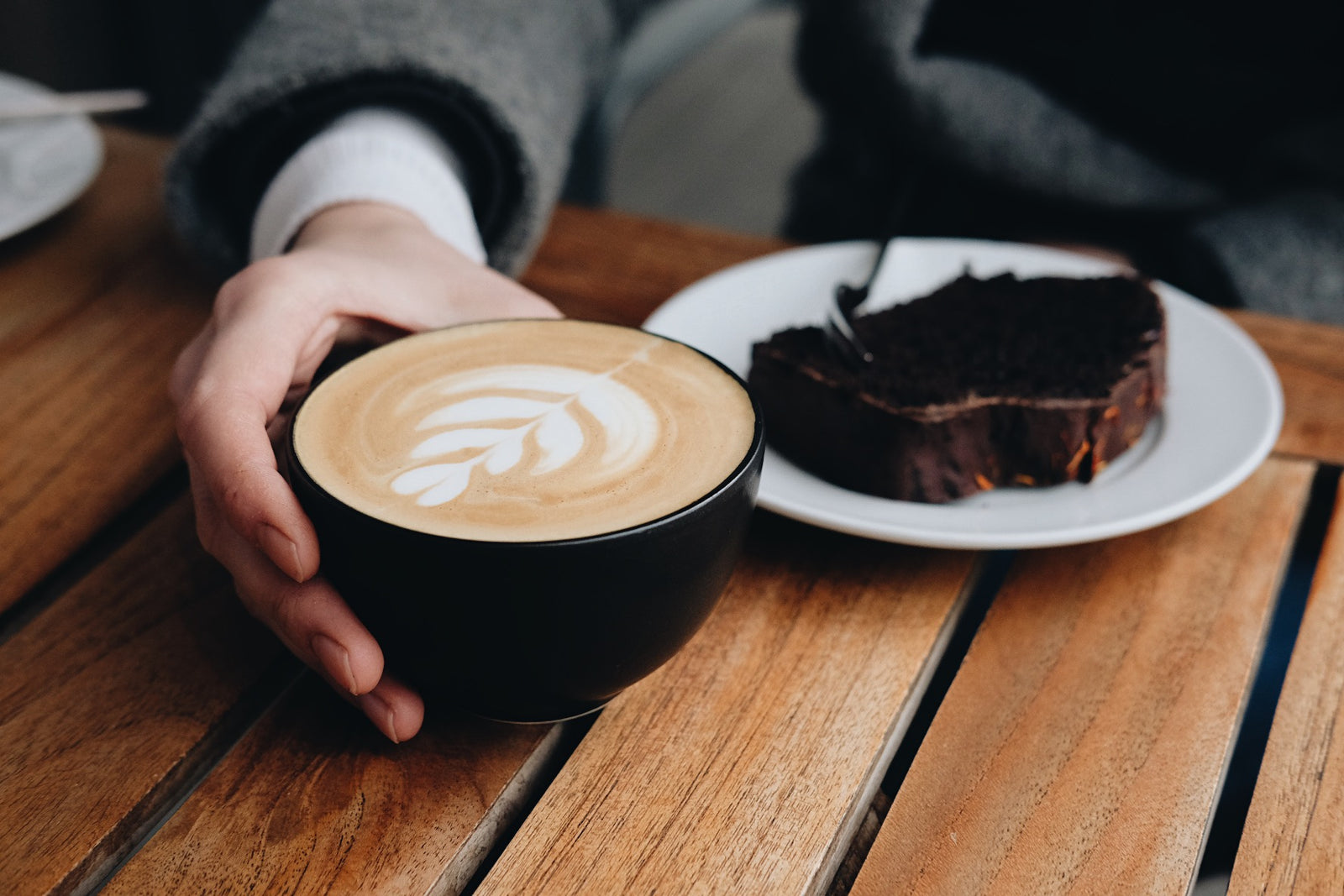 Cappuccino mit Latte Art und ein Stück Schokoladenkuchen auf einem Holztisch