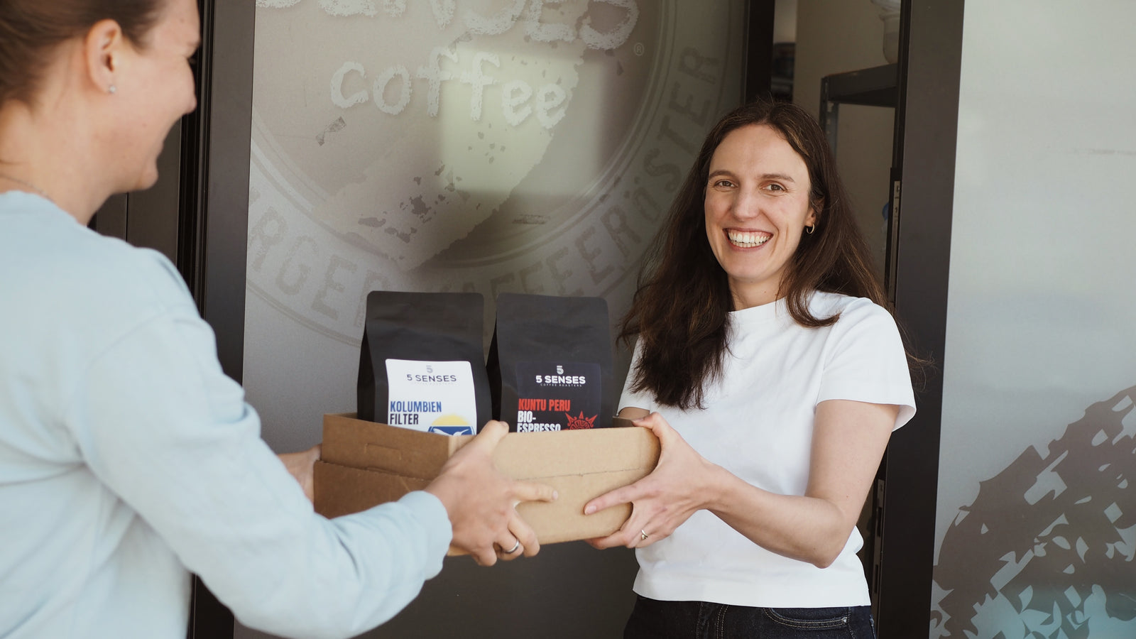 Zwei Personen übergeben eine Kiste mit frisch geröstetem 5 Senses Kaffee